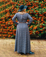 Woman in a long dark dress and black hat standing in front of a wall of orange flowers.. This dress is the Upton Dress & Skirt sewing pattern from Cashmerette.