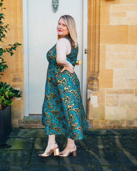 Woman in a teal patterned dress standing in front of a door.. This dress is the Upton Dress & Skirt sewing pattern from Cashmerette.