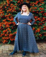 Woman in a blue dress standing in front of a hedge with red flowers. This dress is the Upton Dress & Skirt sewing pattern from Cashmerette.