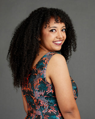 Woman with curly hair wearing a floral dress against a gray background. This dress is the Upton Dress & Skirt sewing pattern from Cashmerette.