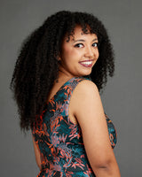 Woman with curly hair wearing a floral dress against a gray background. This dress is the Upton Dress & Skirt sewing pattern from Cashmerette.