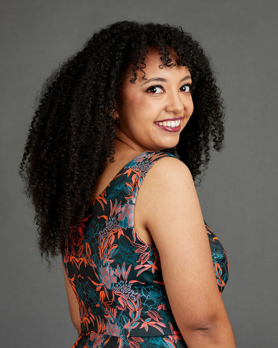 Woman with curly hair wearing a floral dress against a gray background. This dress is the Upton Dress & Skirt sewing pattern from Cashmerette.