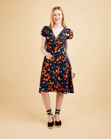 Woman wearing a patterned dress on a beige background. This dress is the Roseclair Wrap Dress sewing pattern from Cashmerette.