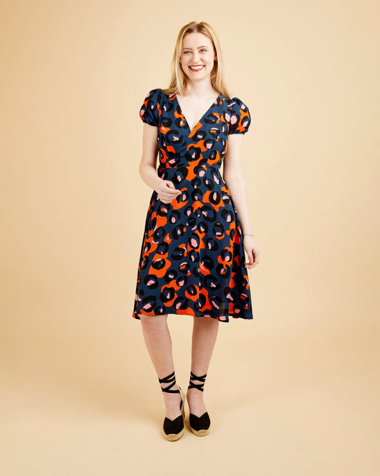 Woman wearing a patterned dress on a beige background. This dress is the Roseclair Wrap Dress sewing pattern from Cashmerette.