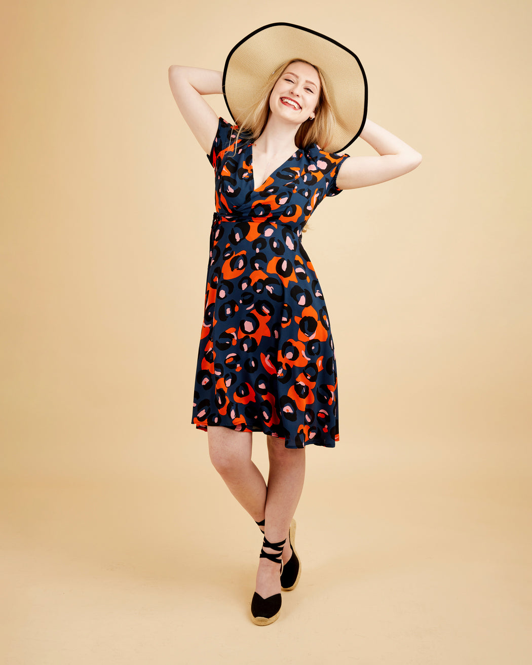 Woman wearing a patterned dress and wide-brimmed hat on a beige background. This dress is the Roseclair Wrap Dress sewing pattern from Cashmerette.