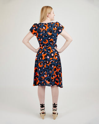 Woman wearing a patterned dress on a plain background. This dress is the Roseclair Wrap Dress sewing pattern from Cashmerette.