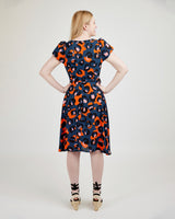 Woman wearing a patterned dress on a plain background. This dress is the Roseclair Wrap Dress sewing pattern from Cashmerette.