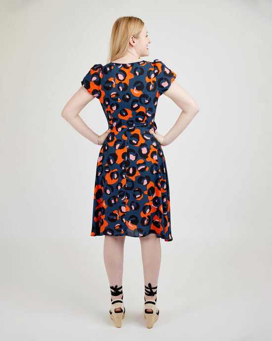 Woman wearing a patterned dress on a plain background. This dress is the Roseclair Wrap Dress sewing pattern from Cashmerette.
