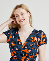 Woman wearing a blue dress with orange and pink abstract pattern on a plain background. This dress is the Roseclair Wrap Dress sewing pattern from Cashmerette.