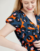 Woman wearing a blue dress with orange and black abstract pattern. This dress is the Roseclair Wrap Dress sewing pattern from Cashmerette.