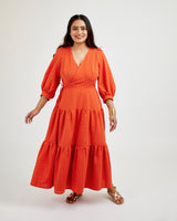 Woman wearing a red dress with a white background. This dress is the Roseclair Wrap Dress sewing pattern from Cashmerette.