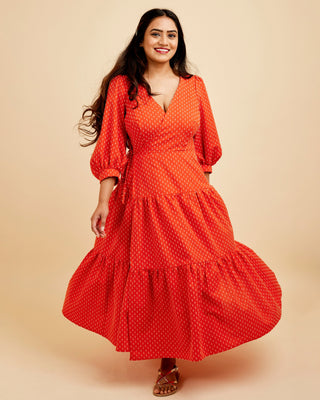 Woman wearing a red polka dot dress on a beige background. This dress is the Roseclair Wrap Dress sewing pattern from Cashmerette.