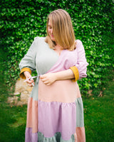 Woman in a layered outfit with a green background. This dress is the Roseclair Wrap Dress sewing pattern from Cashmerette.