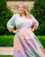 Woman wearing a colorful dress with a green, pink, and purple pattern standing outdoors.This dress is the Roseclair Wrap Dress sewing pattern from Cashmerette.