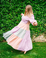 Woman in a pastel-colored dress twirling in front of a green hedge.. This dress is the Roseclair Wrap Dress sewing pattern from Cashmerette.