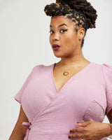 Woman wearing a pink dress against a white background. This dress is the Roseclair Wrap Dress sewing pattern from Cashmerette.