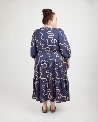 Woman wearing a navy dress with pink wavy patterns on a white background. This dress is the Roseclair Wrap Dress sewing pattern from Cashmerette.