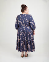 Woman wearing a navy dress with pink wavy patterns on a white background. This dress is the Roseclair Wrap Dress sewing pattern from Cashmerette.