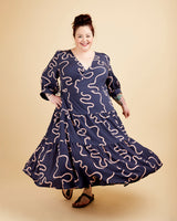 Woman wearing a navy dress with pink patterns on a beige background. This dress is the Roseclair Wrap Dress sewing pattern from Cashmerette.