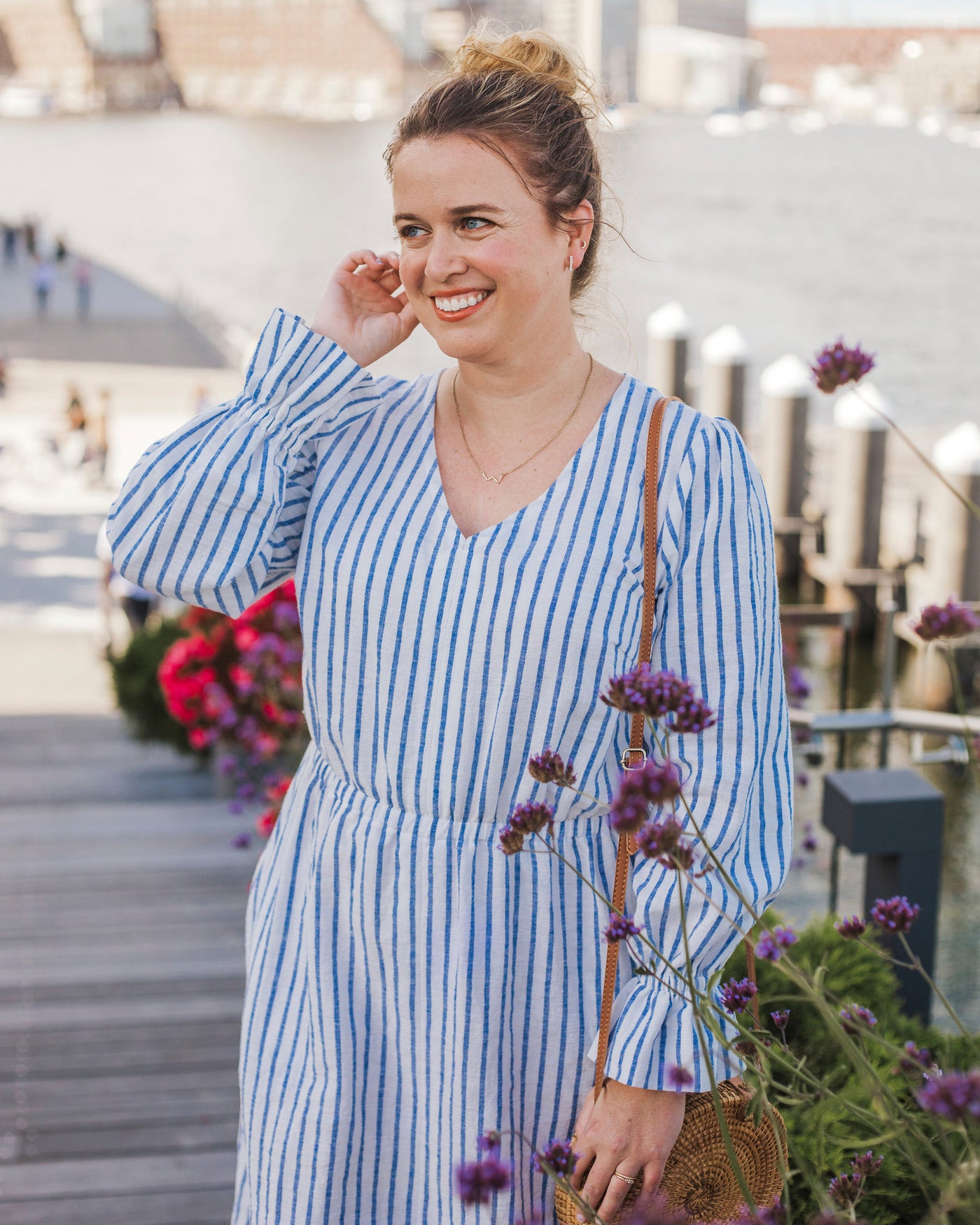 Woman in a blue striped dress standing outdoors with flowers and a blurred background. This dress is the Kineton Dress & Top sewing pattern from Cashmerette.