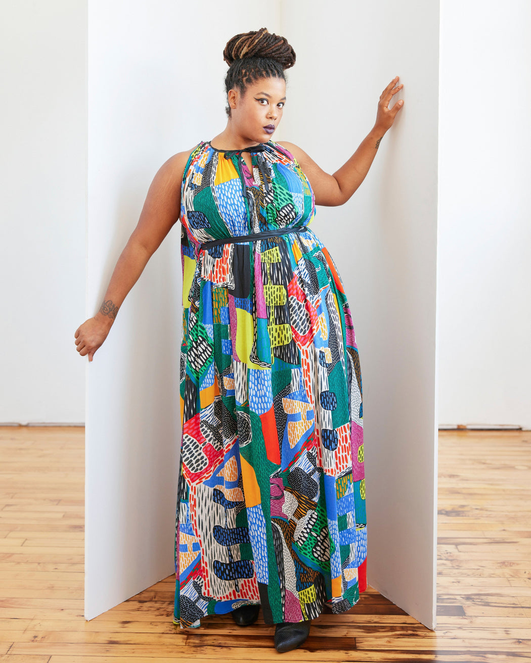 Woman wearing a colorful patterned dress standing against a white wall. This dress is the Rockwell Dress sewing pattern from Cashmerette.