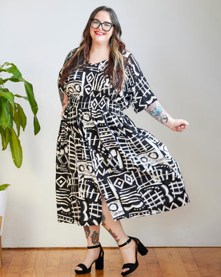 Woman wearing a black and white patterned dress standing indoors with a plant in the background. This dress is the Franconia Dress sewing pattern from Cashmerette.