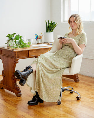 Woman sitting in a chair holding a phone in a room with a desk and plants. This dress is the Hampden Dress sewing pattern from Cashmerette.