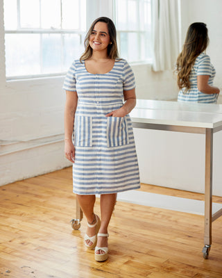 Woman wearing a blue and white striped dress in a bright room with large windows. This dress is the Hampden Dress sewing pattern from Cashmerette.