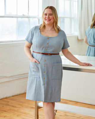 Woman wearing a blue dress with a brown belt in a bright room. This dress is the Hampden Dress sewing pattern from Cashmerette.