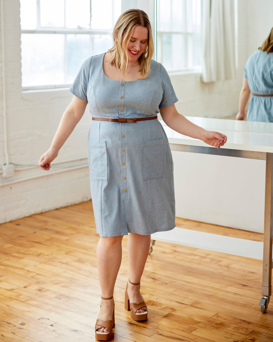 Woman wearing a light blue dress standing in a room with wooden floor and large windows. This dress is the Hampden Dress sewing pattern from Cashmerette.