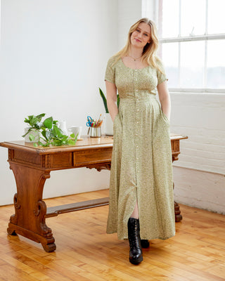 Woman in a long green dress standing in a room with wooden floors and a large window. This dress is the Hampden Dress sewing pattern from Cashmerette.