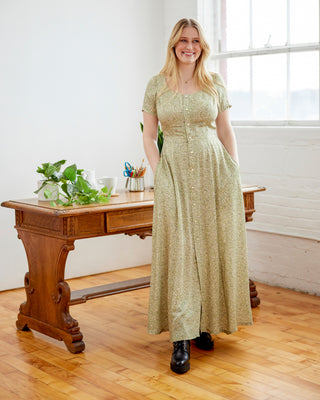 Woman in a long green dress standing in a room with wooden floors and a large window. This dress is the Hampden Dress sewing pattern from Cashmerette.