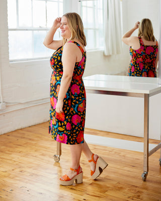 Woman in a colorful dress standing in a room with wooden floor and white walls. This dress is the Hampden Dress sewing pattern from Cashmerette.
