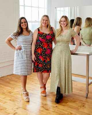 Three women in dresses standing in a room with wooden flooring and large windows. This dress is the Hampden Dress sewing pattern from Cashmerette.