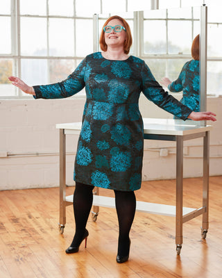 Woman wearing a blue patterned dress standing in front of a mirror. This dress is the Wyman Dress Sloper sewing pattern from Cashmerette.