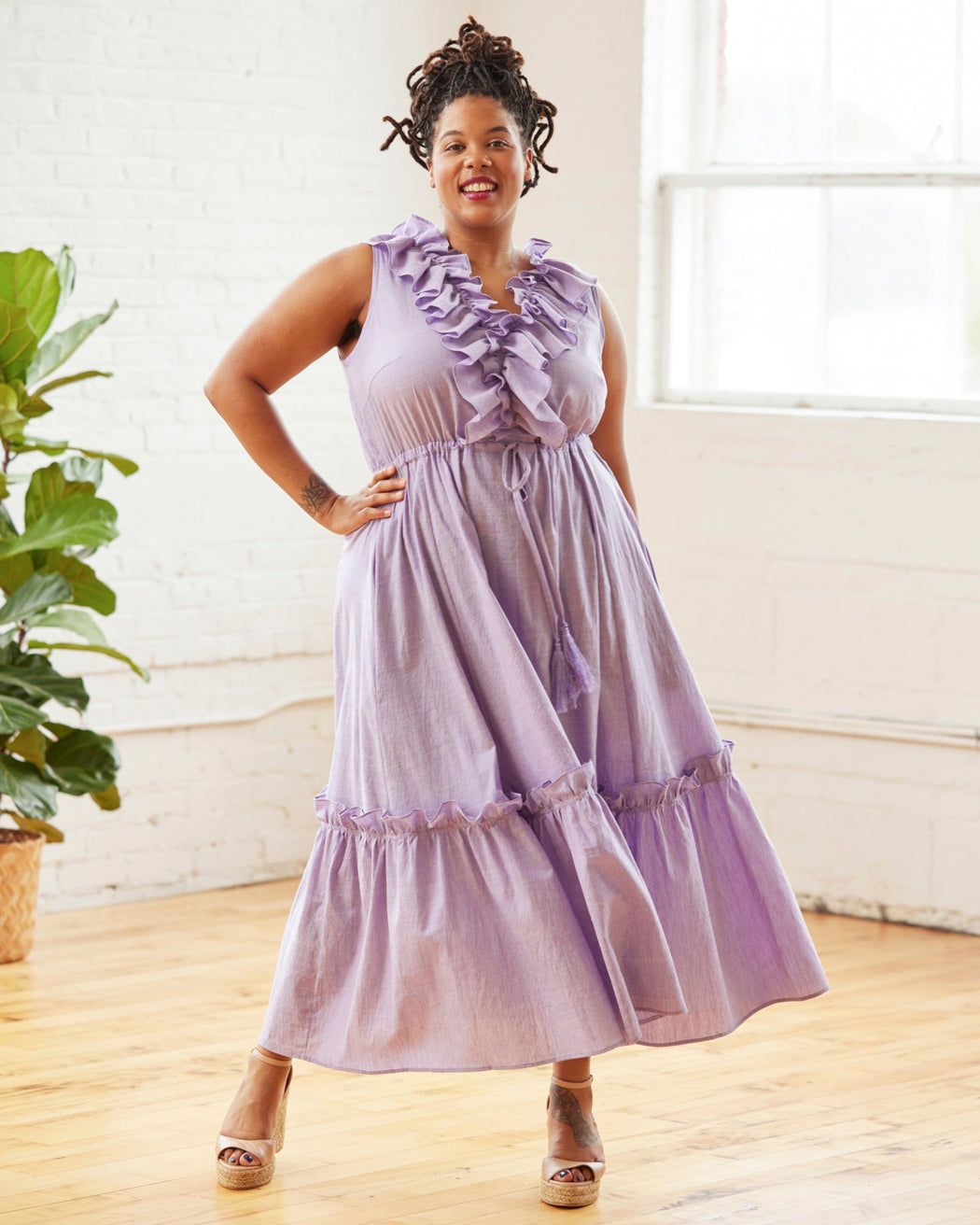 Woman wearing a purple dress with ruffles in a bright room. This dress is the Loring Dress sewing pattern from Cashmerette.