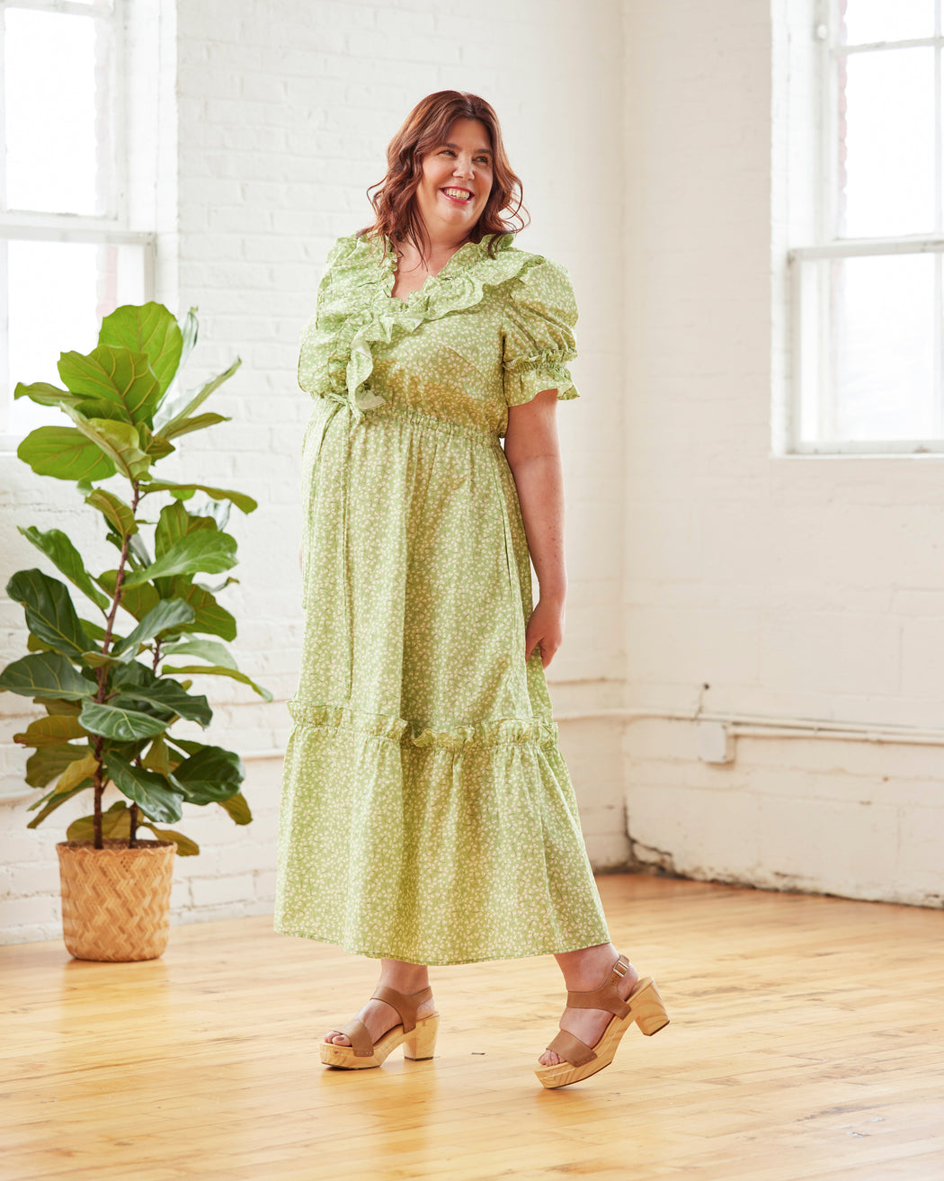 Woman in a green dress standing in a room with a plant and white walls. This dress is the Loring Dress sewing pattern from Cashmerette.