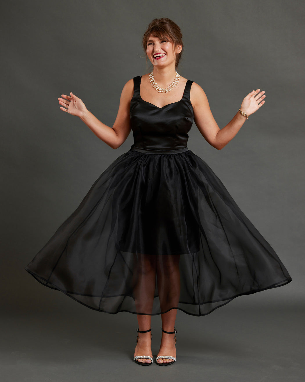 Woman wearing a black dress against a gray background. This dress is the Mansfield Dress sewing pattern from Cashmerette.