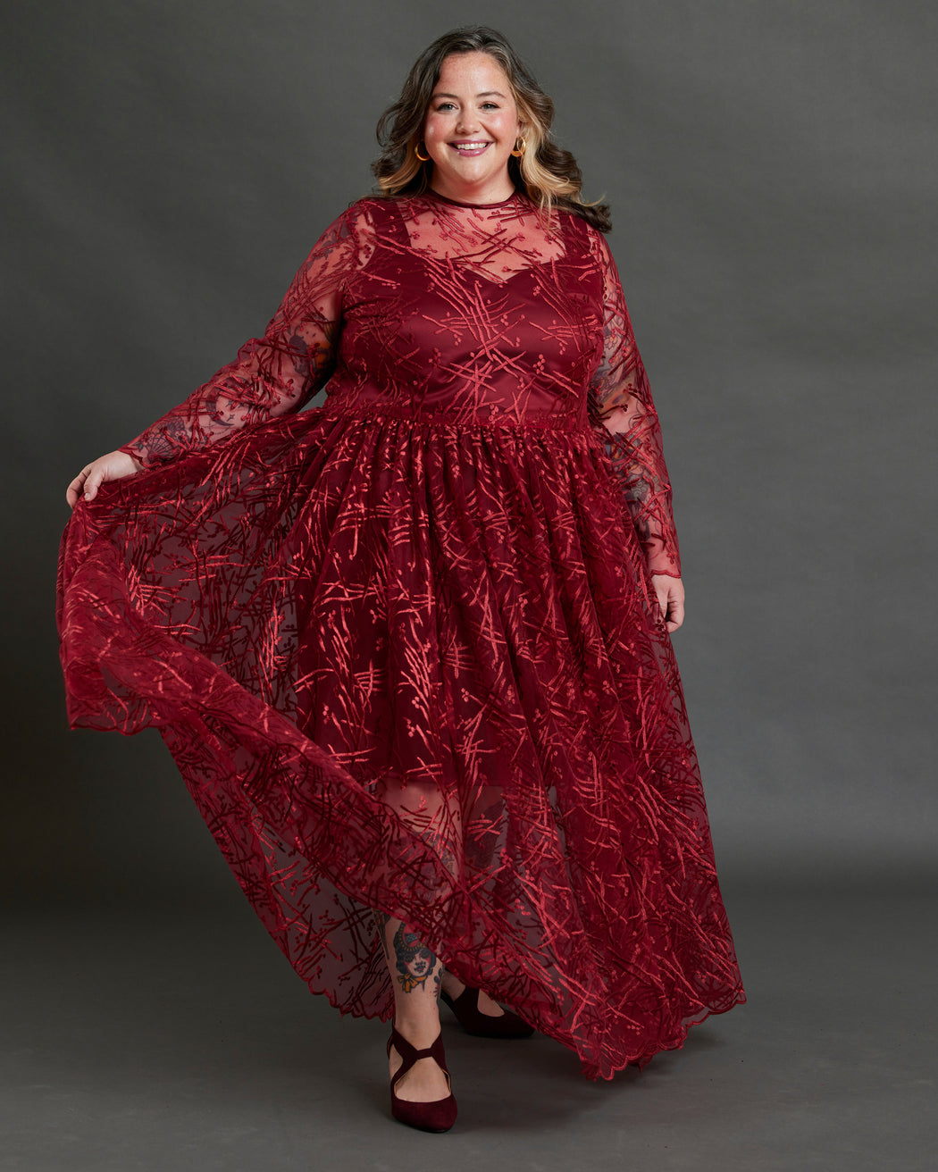 Woman wearing a red lace dress against a gray background. This dress is the Mansfield Dress sewing pattern from Cashmerette.
