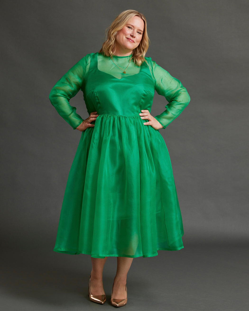 Woman wearing a green dress against a gray background. This dress is the Mansfield Dress sewing pattern from Cashmerette.