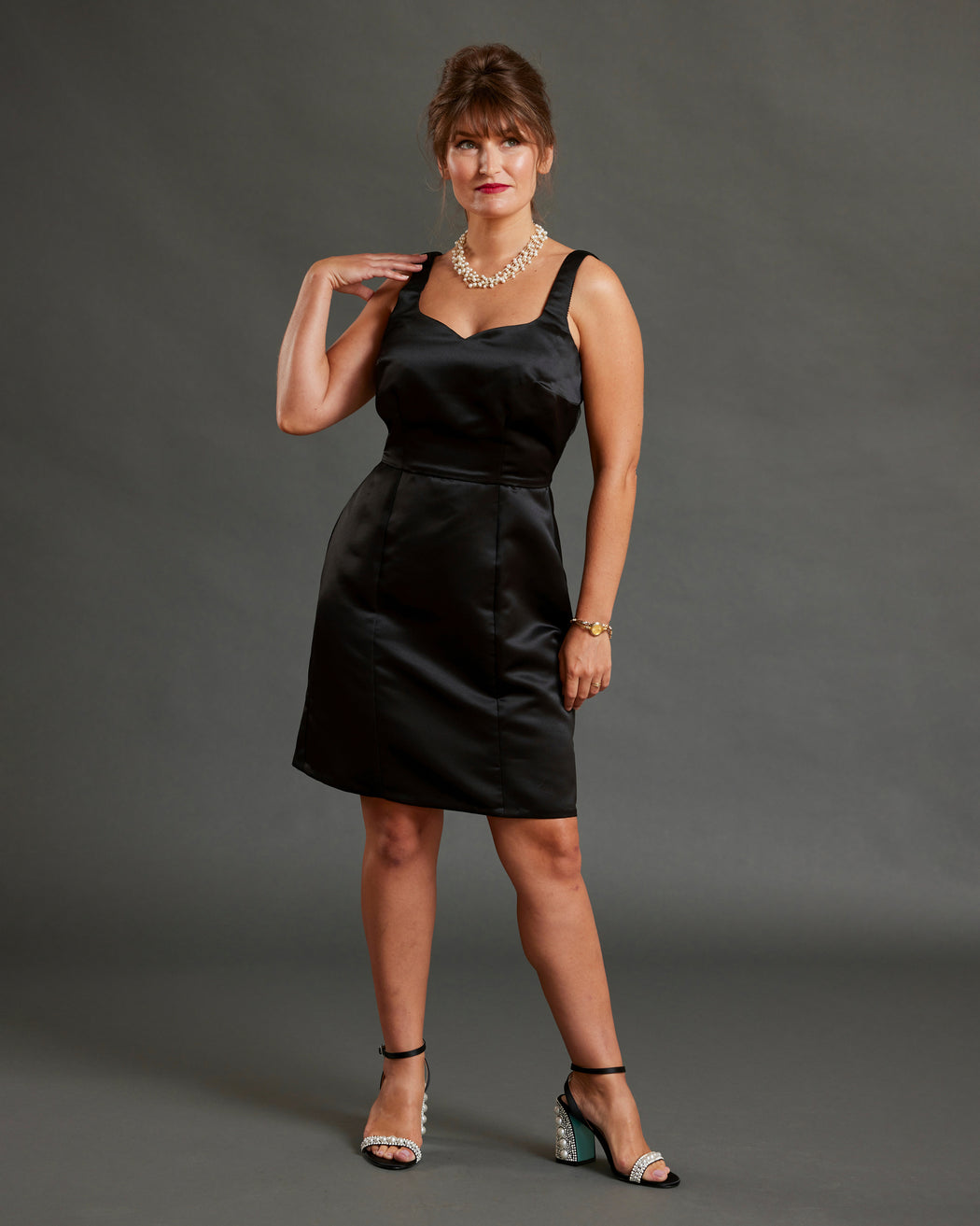 Woman wearing a black dress against a gray background. This dress is the Mansfield Dress sewing pattern from Cashmerette.