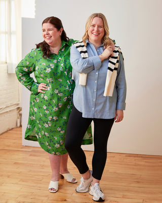 Two women standing together, one wearing a green floral dress and the other in a blue shirt and black leggings, holding a striped scarf. This dress is the Winvale Dress & Tunic sewing pattern from Cashmerette.