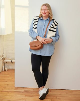 Woman wearing a blue shirt, black leggings, striped vest, and carrying a brown bag indoors. This dress is the Winvale Dress & Tunic sewing pattern from Cashmerette.