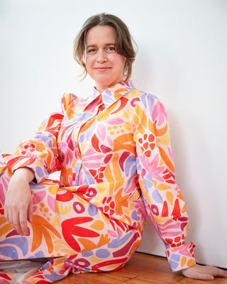 Woman wearing a colorful floral dress sitting on the floor against a white wall. This dress is the Winvale Dress & Tunic sewing pattern from Cashmerette.