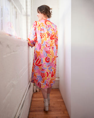 Woman wearing a colorful floral dress standing in a room with white walls and wooden floor. This dress is the Winvale Dress & Tunic sewing pattern from Cashmerette.