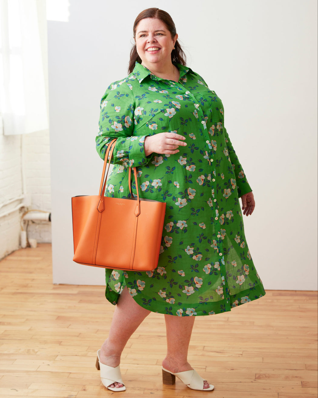 Woman wearing a green floral dress holding an orange handbag indoors. This dress is the Winvale Dress & Tunic sewing pattern from Cashmerette.