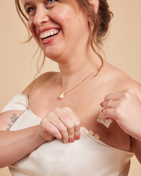 Woman wearing a gold necklace with a pearl pendant against a beige background. This dress is the Ellington Strapless Dress sewing pattern from Cashmerette.
