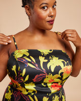 Woman wearing a black dress with colorful floral patterns on a beige background. This dress is the Ellington Strapless Dress sewing pattern from Cashmerette.