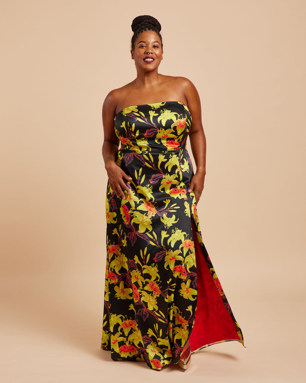 Woman wearing a strapless floral dress with a red lining on a beige background. This dress is the Ellington Strapless Dress sewing pattern from Cashmerette.