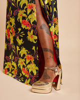 Gold high-heeled shoes with a colorful floral-patterned skirt on a beige background. This dress is the Ellington Strapless Dress sewing pattern from Cashmerette.